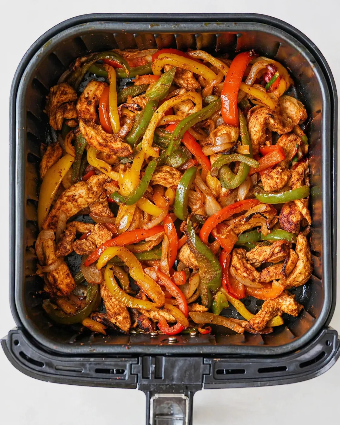 colorful sautéed chicken with bell peppers and onions in a black air fryer basket