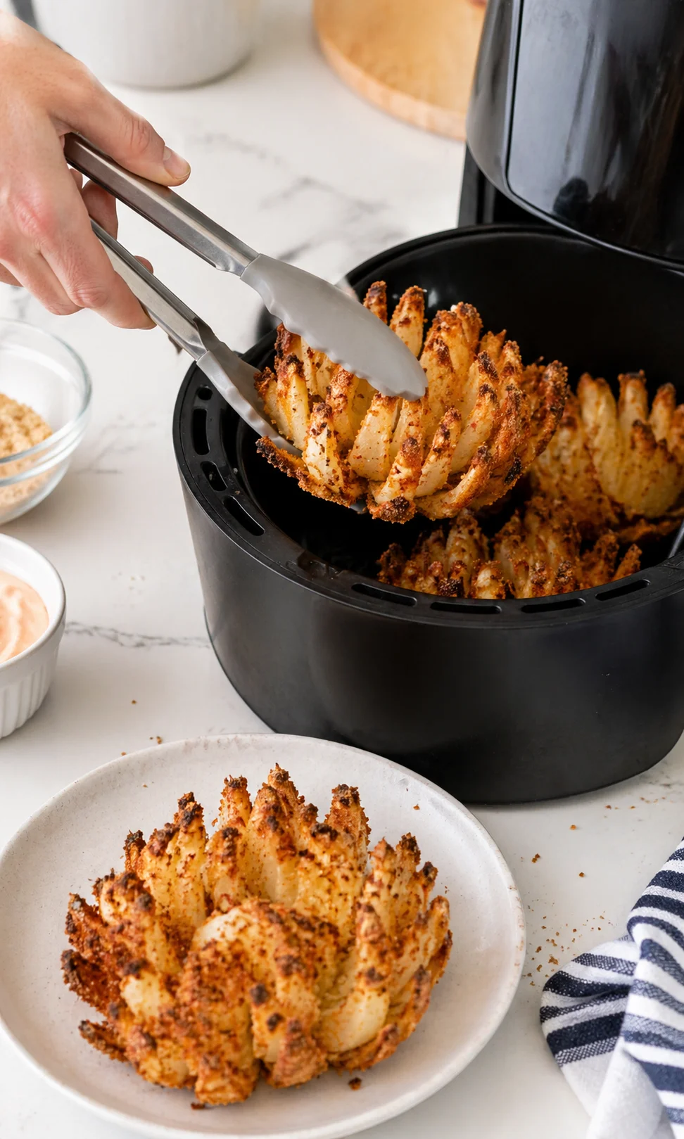 Golden-brown spiral potato rosettes being lifted from a black air fryer basket, plated beside dipping sauces.