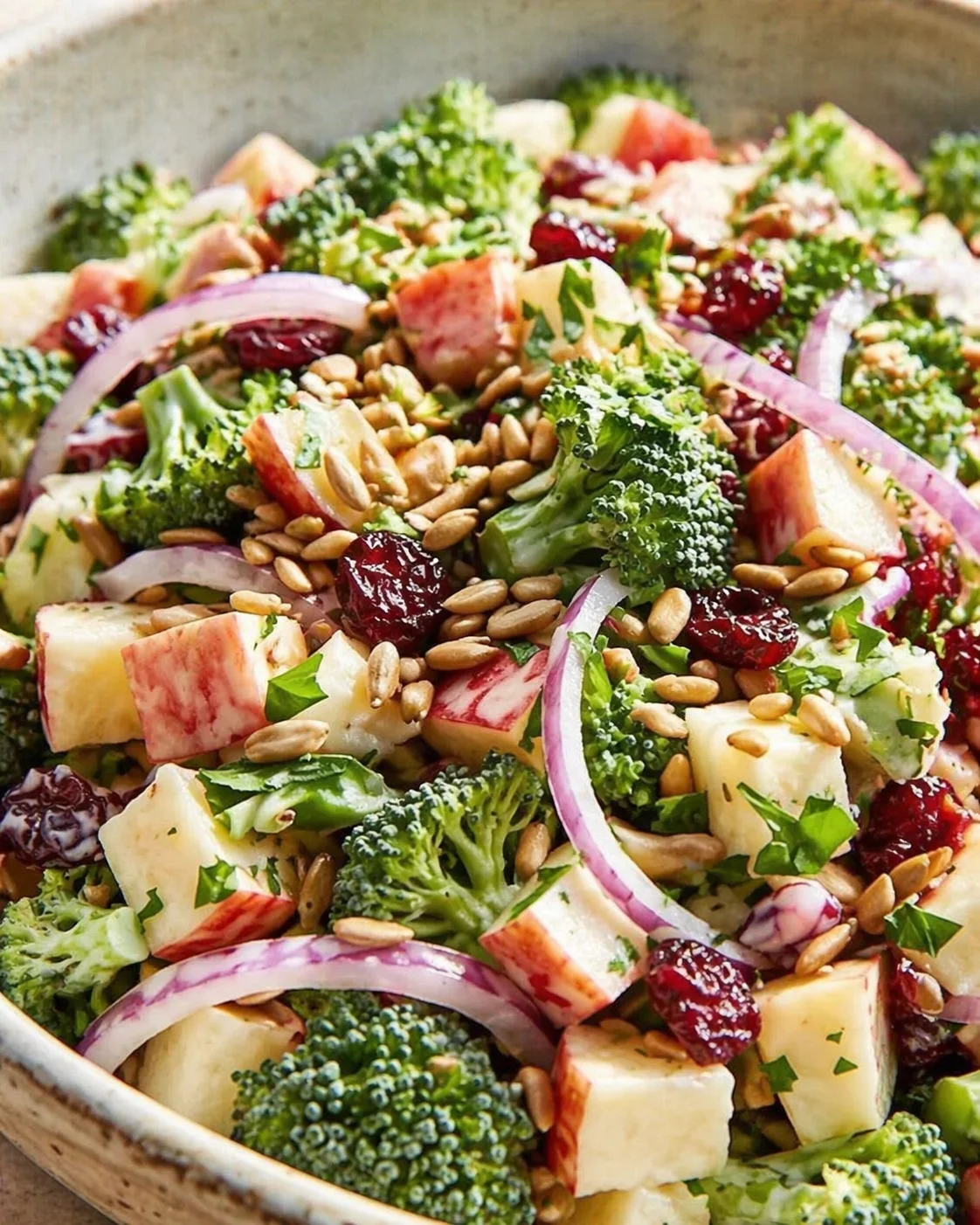 mixed broccoli salad with apple cubes, red onions, dried cranberries, and sunflower seeds in a light dressing