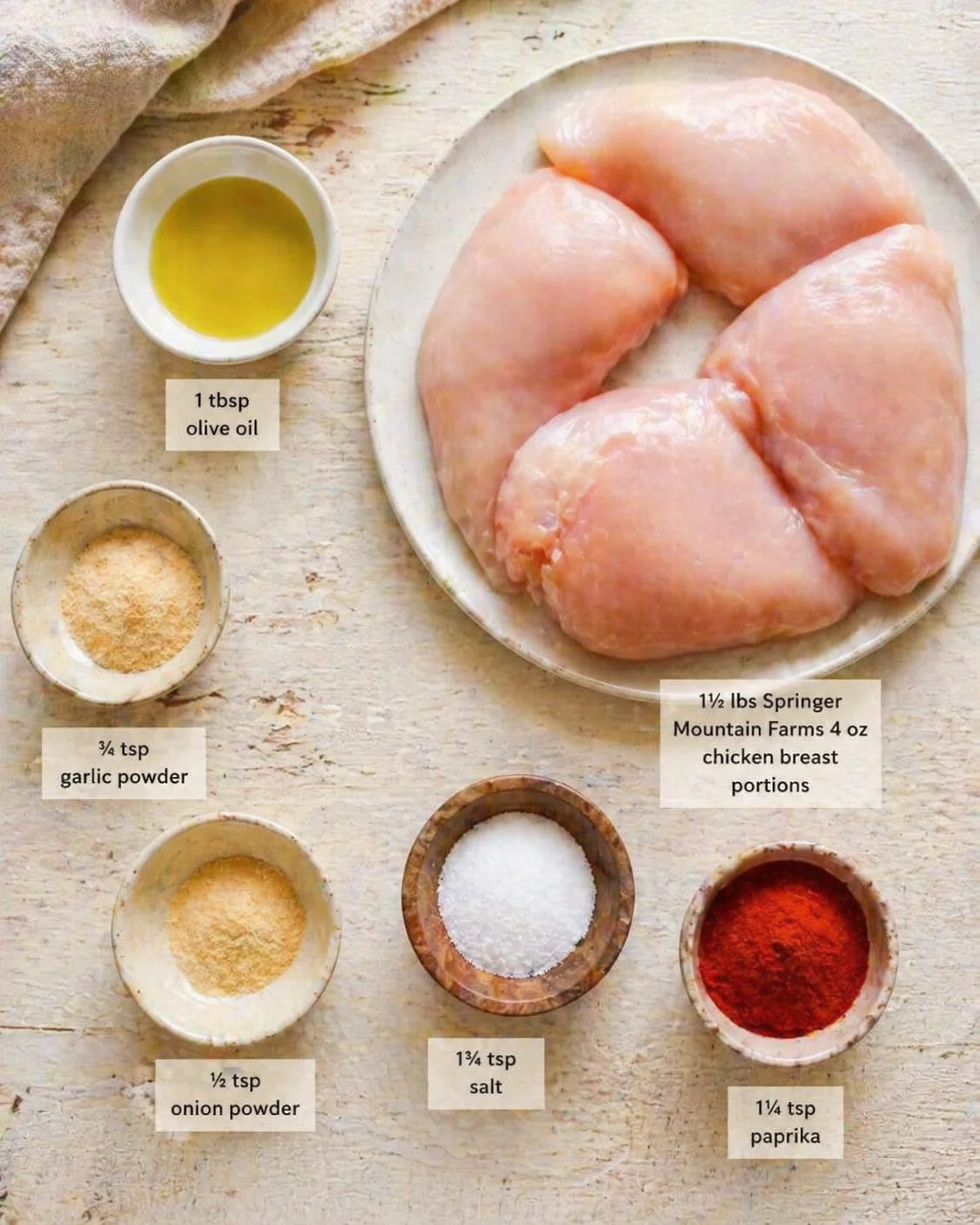 Raw chicken breast portions with olive oil and spice bowls on a rustic wood surface.