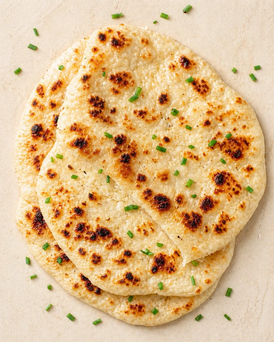 Two overlapping naan-like flatbreads with charred spots, glossy surface, and chopped green chives.