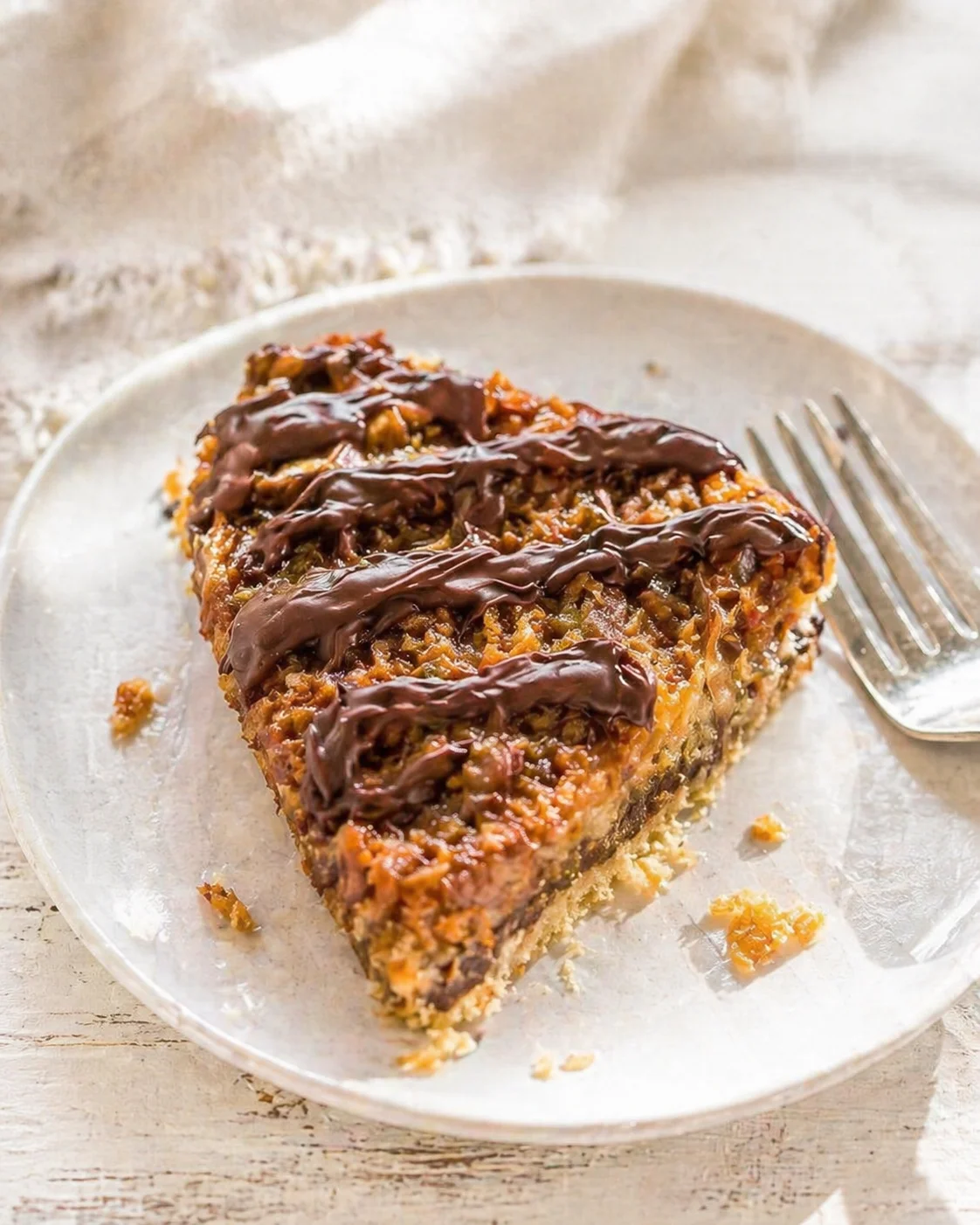 slice of nut-filled chocolate-drizzled cake on a light plate with a fork