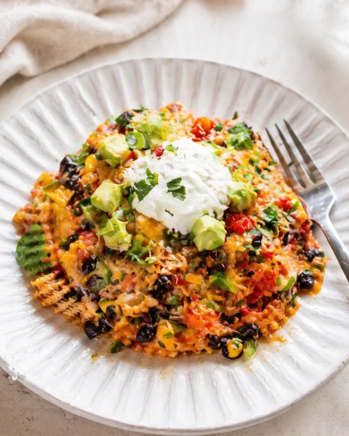Colorful vegetable rice with avocado chunks, black beans, corn, cilantro, and a dollop of sour cream on a white plate.