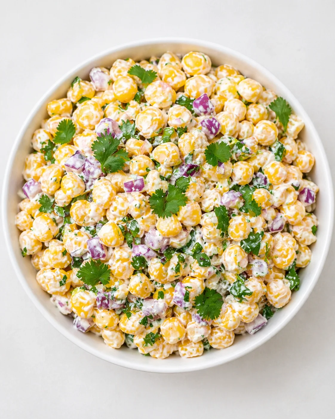 Creamy corn salad with red onion and cilantro in a white bowl