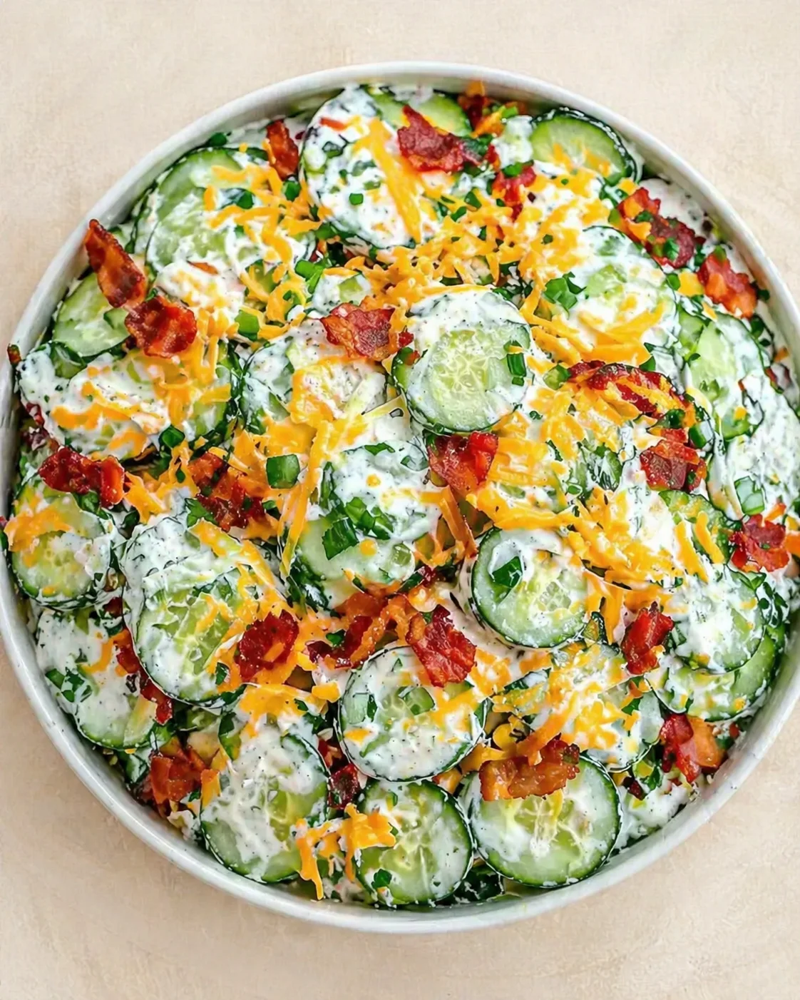 Round baking dish covered with cucumber slices in a creamy ranch-dill sauce, bacon bits, and cheddar.