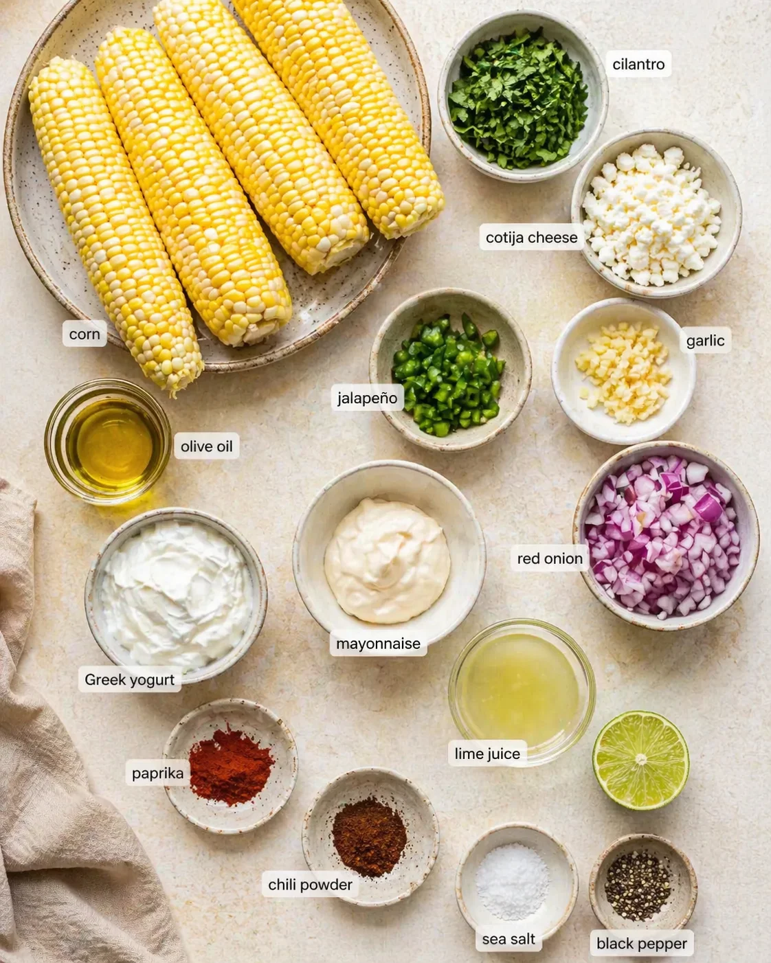 Four ears of corn sit on a plate with bowls of cotija, cilantro, jalapeño, red onion, and sauces.