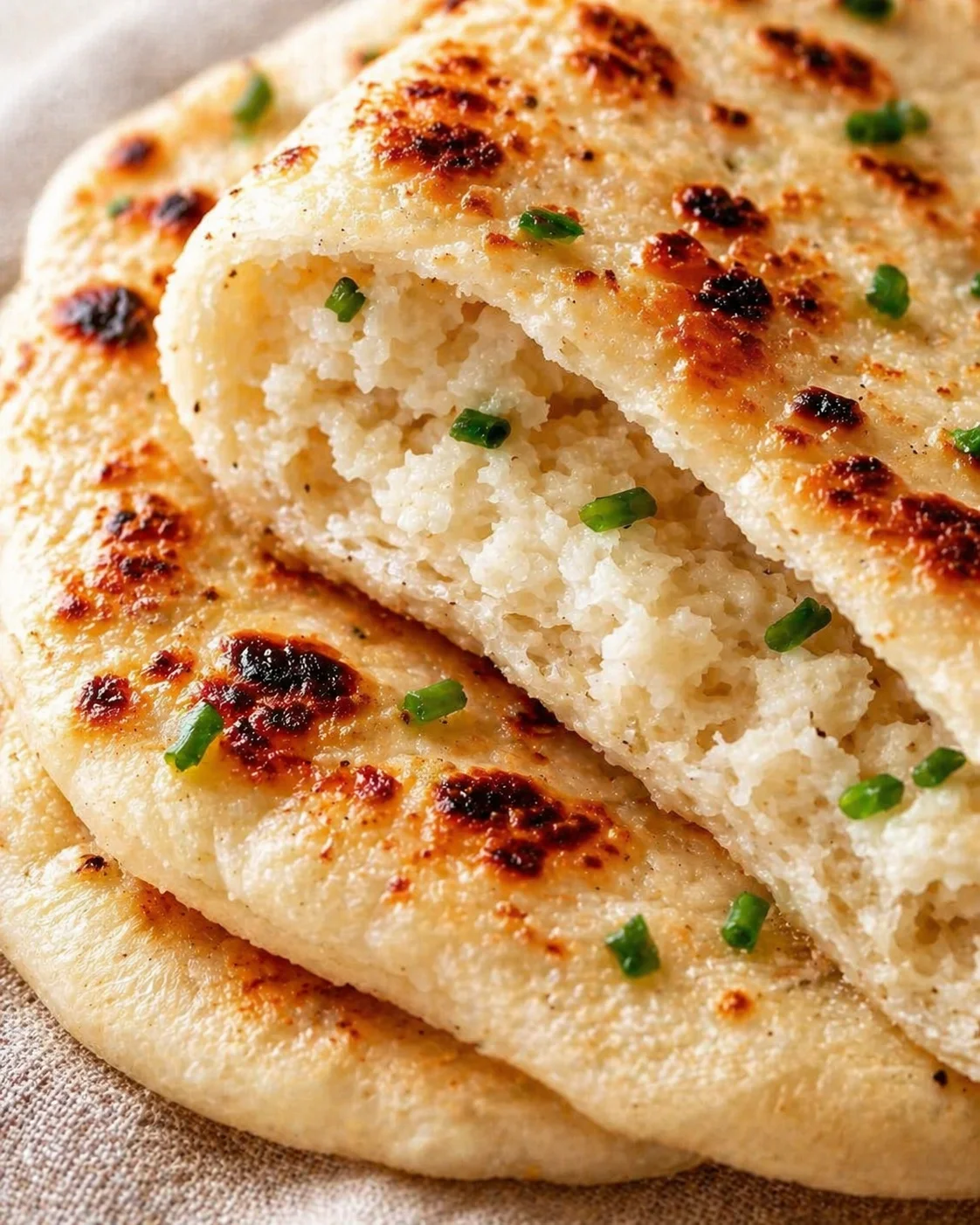 Close-up of flaky naan with browned spots and chopped scallions