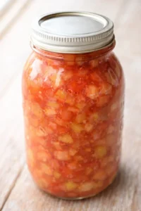 clear glass mason jar filled with chunky tomato salsa on a light wooden surface