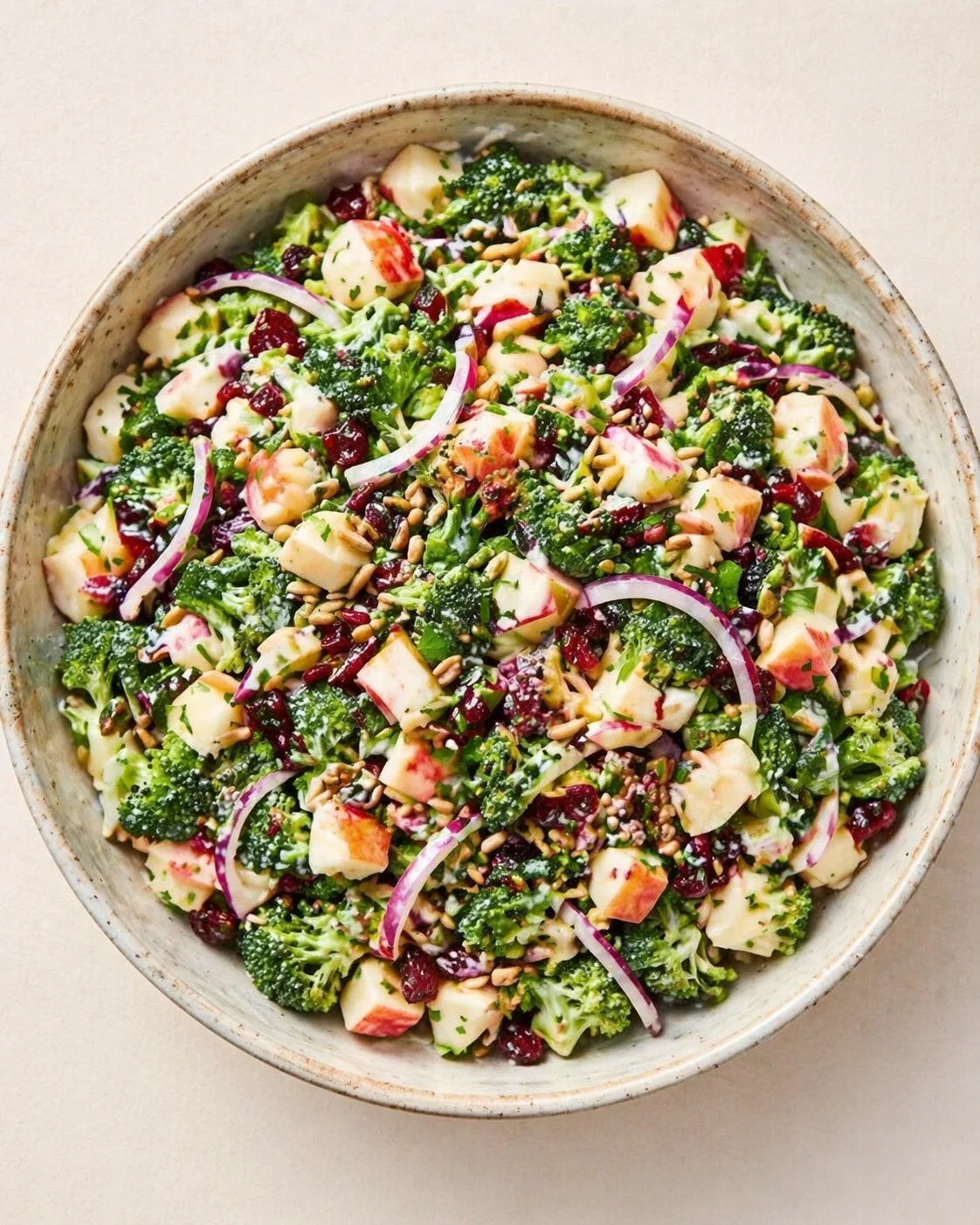 Vibrant kale and apple salad with red onion, cranberries, and pine nuts in a ceramic bowl