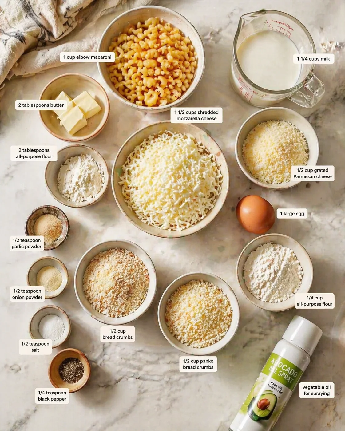 Overhead view of macaroni ingredients arranged in labeled bowls on marble surface.