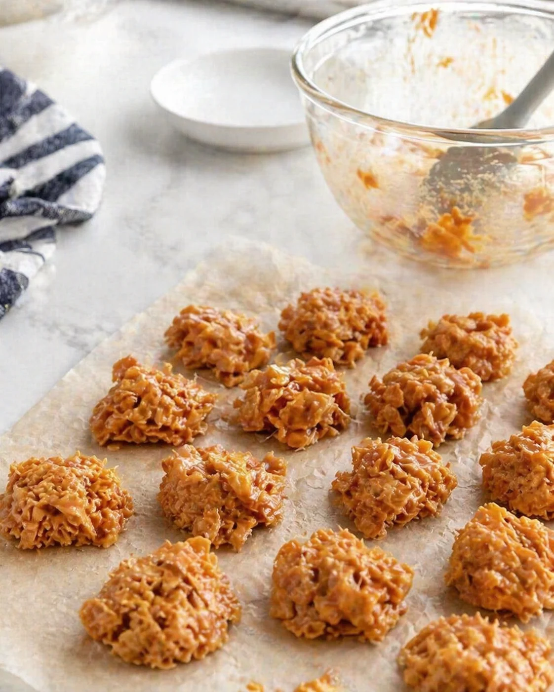 Small no bake energy bites arranged on parchment with a mixing bowl in the background.