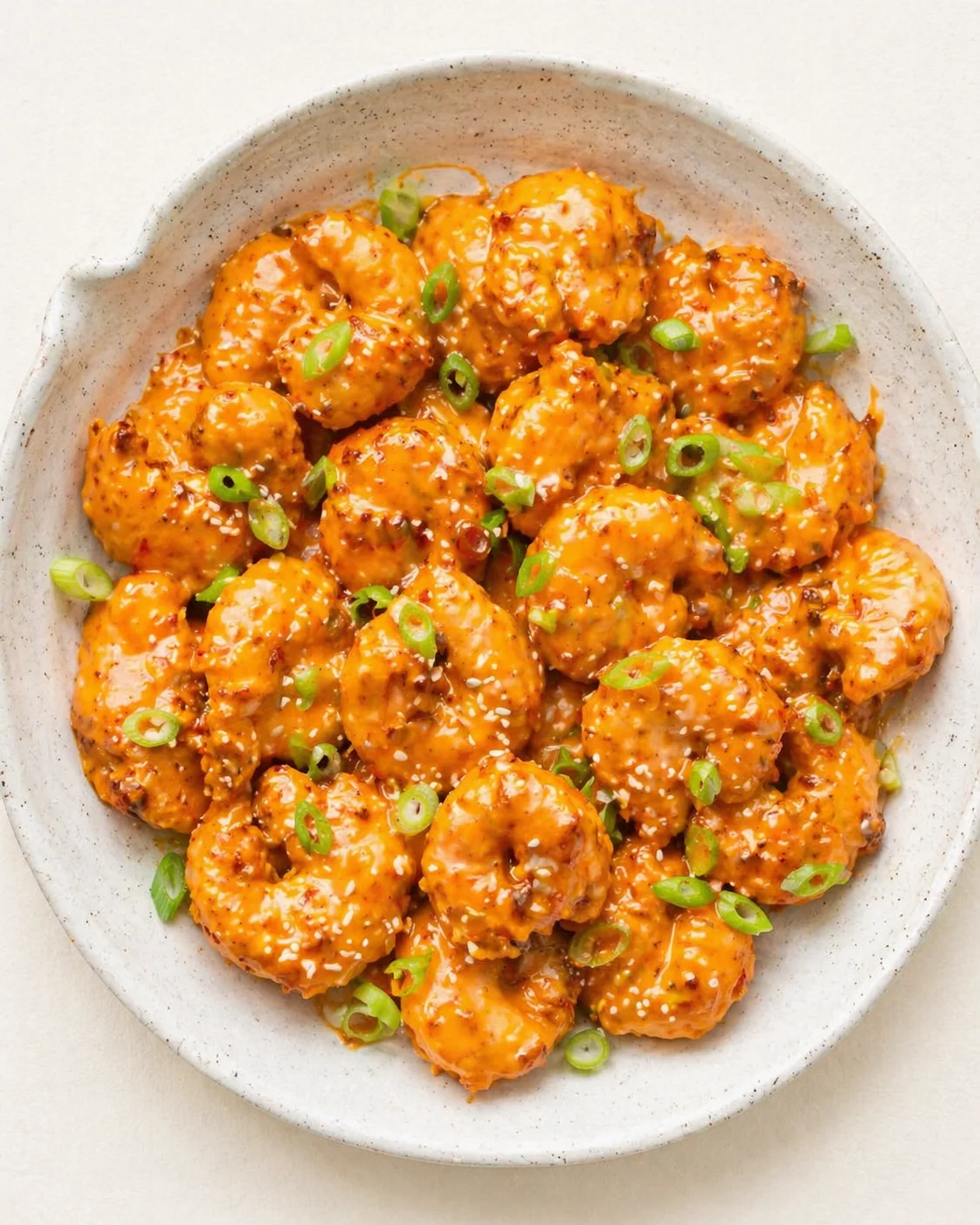 orange-glazed chicken bites with sesame seeds and green onions in a speckled bowl