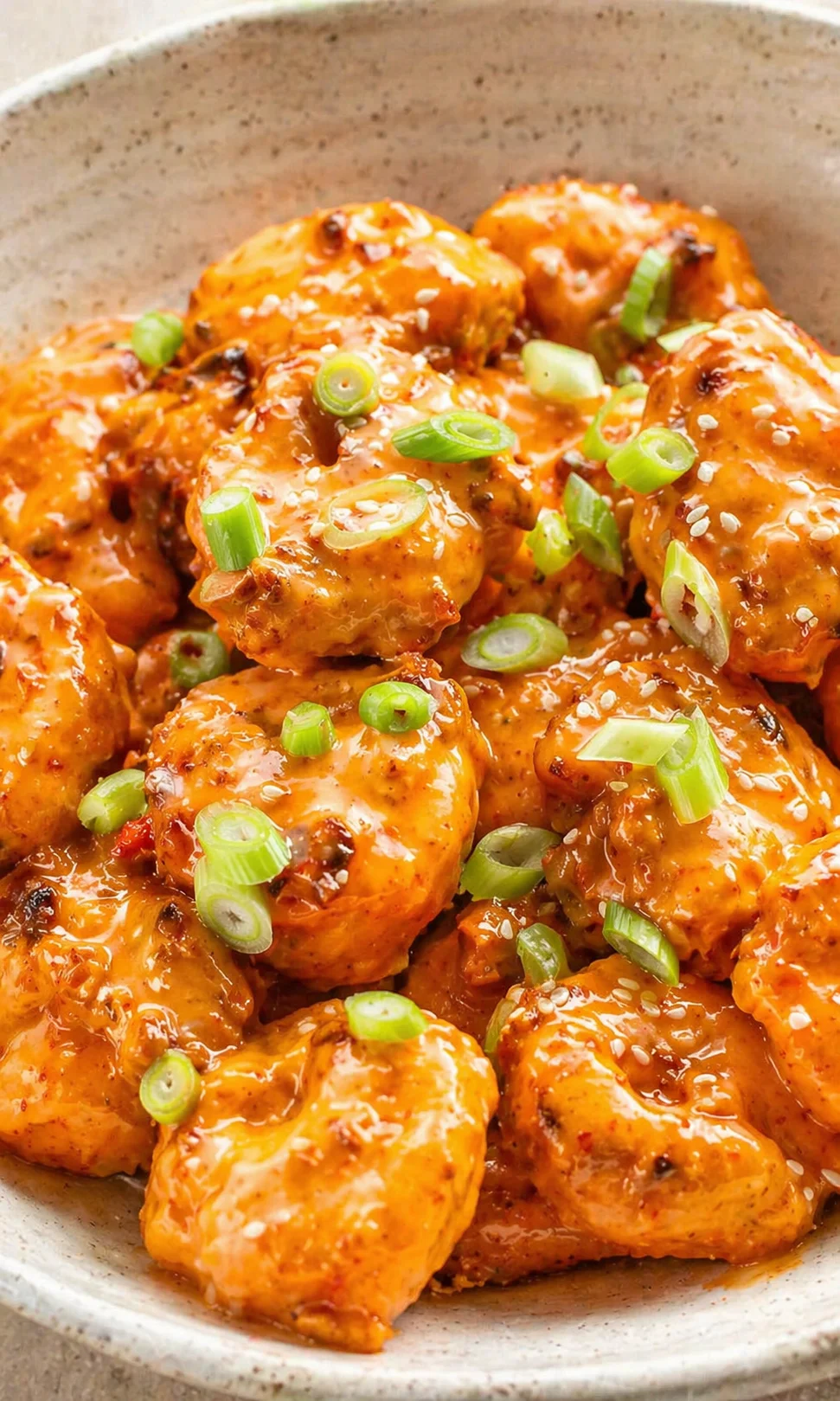 Close-up of orange-glazed chicken meatballs in a speckled bowl, topped with sesame seeds and green onions.