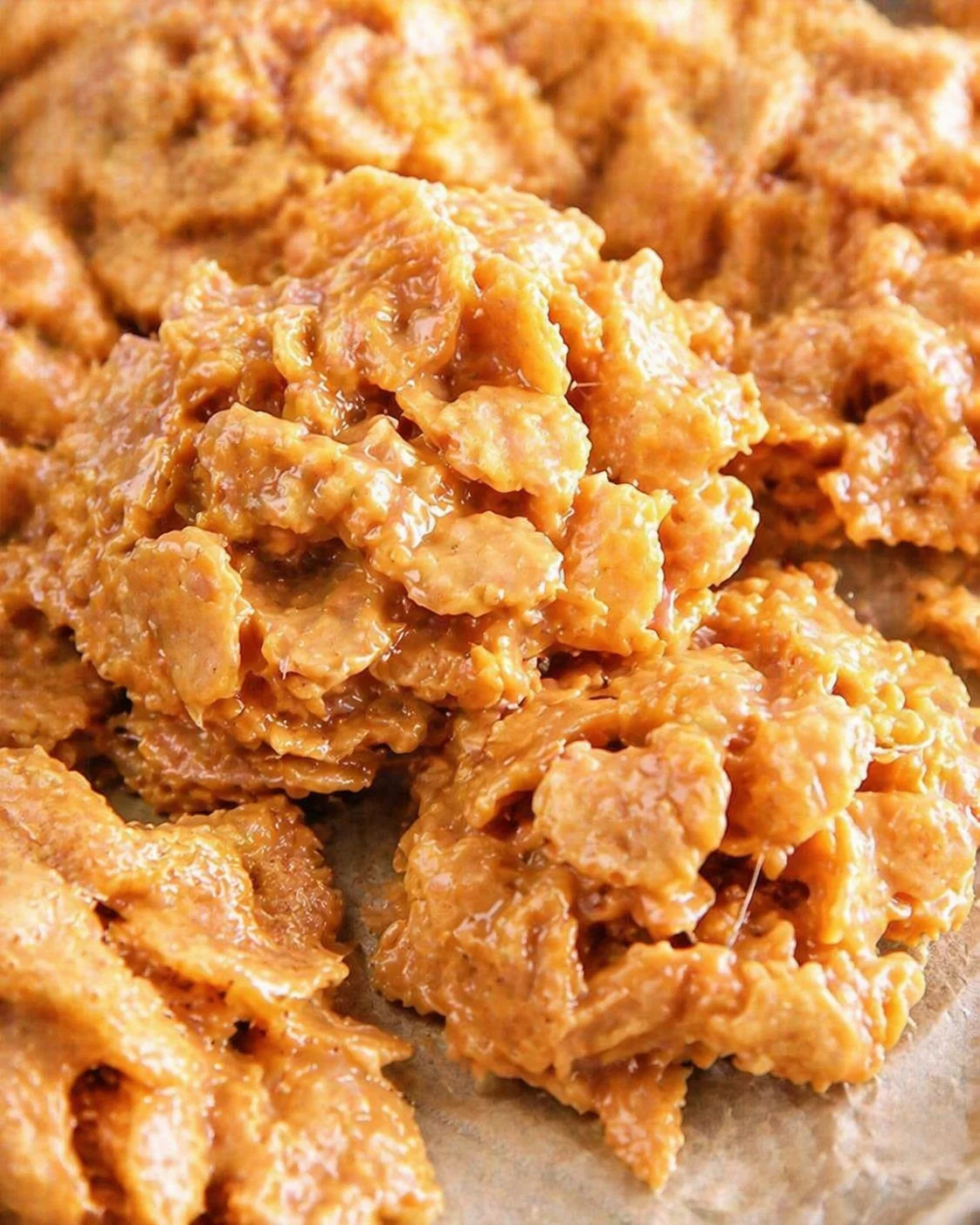 Sticky orange peanut butter clusters on parchment with glossy caramel coating