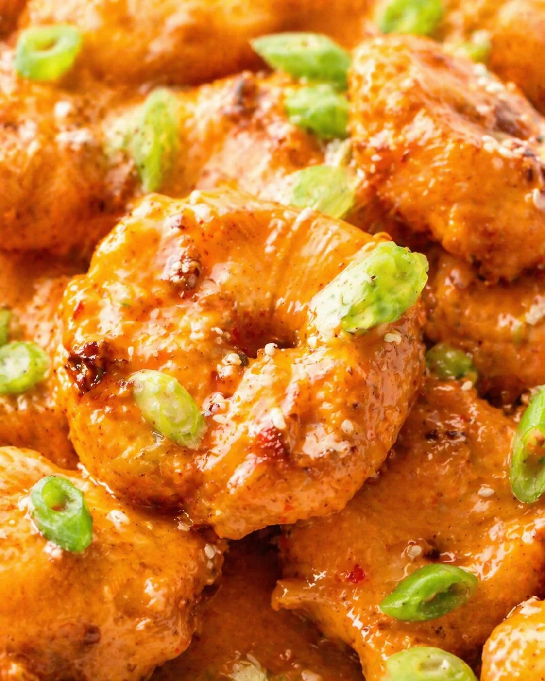 Close-up of crispy orange-glazed chicken bites topped with sesame seeds and green onions.