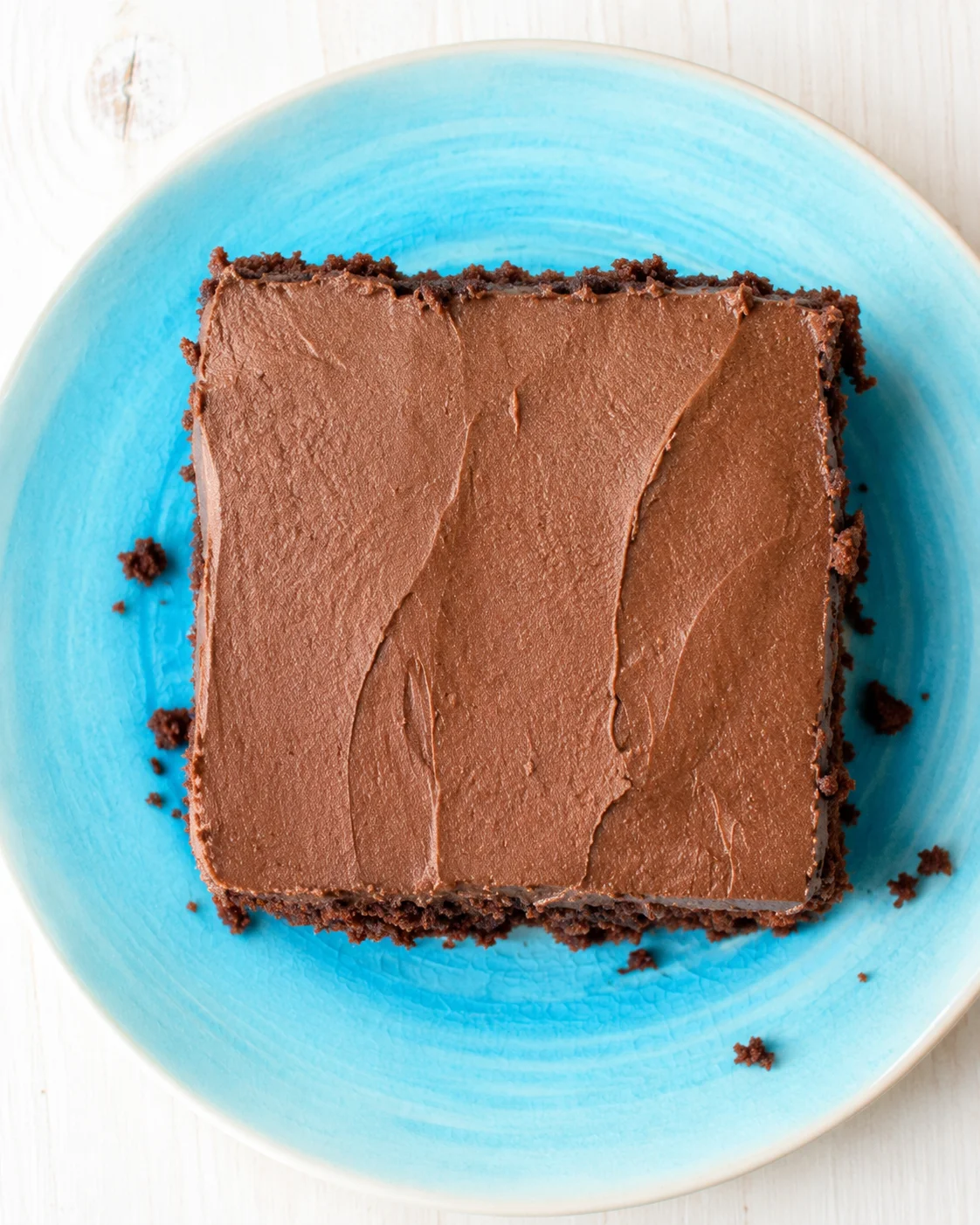 square chocolate brownie with smooth glossy frosting on a bright blue plate