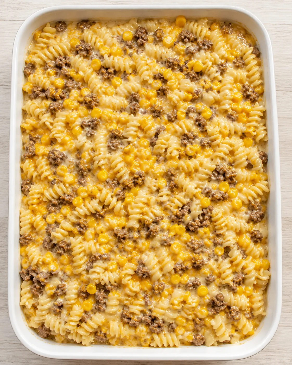 top-down view of a white baking dish filled with fusilli pasta, ground beef, corn in a creamy cheese sauce