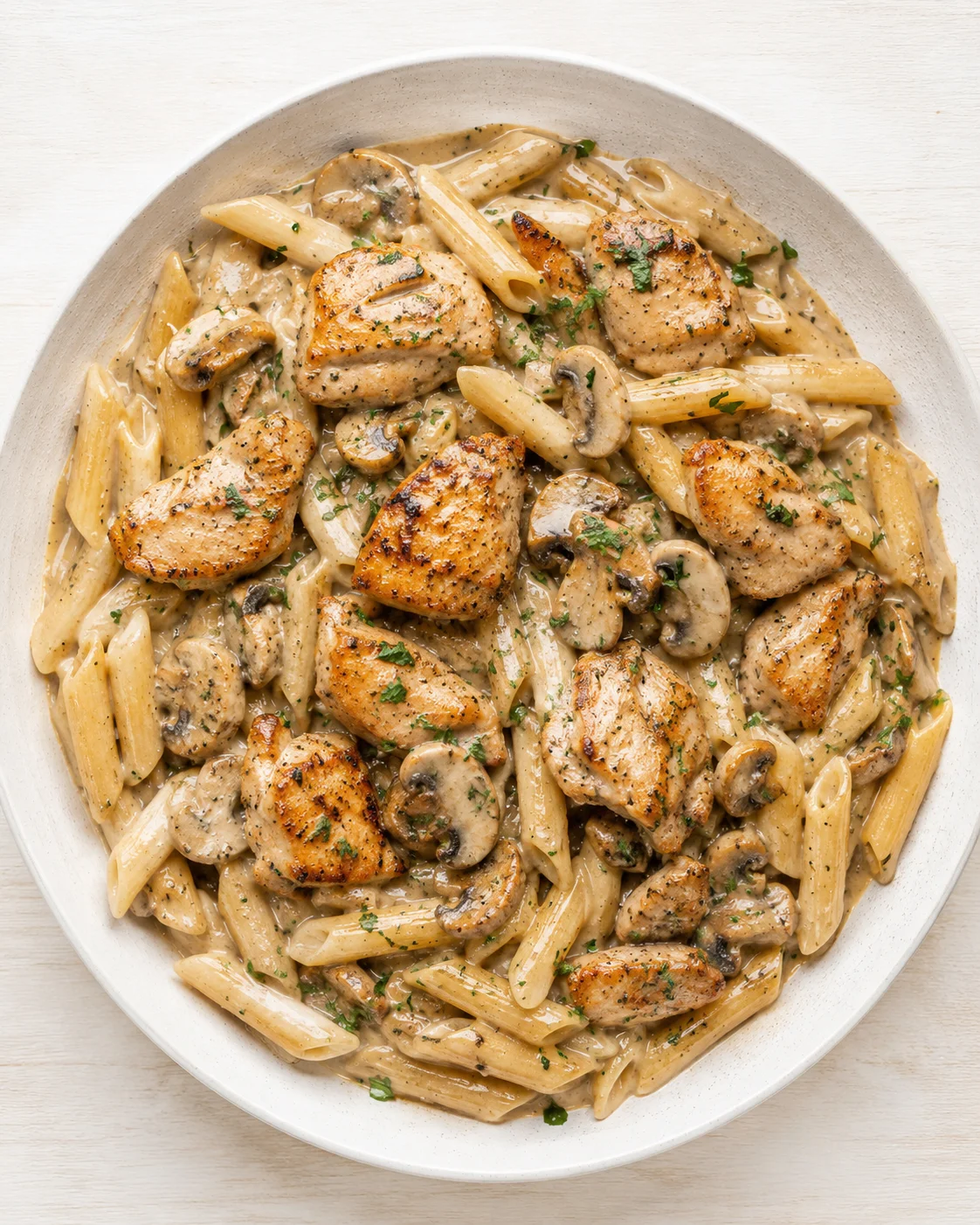 Overhead view of creamy mushroom chicken pasta with seared chicken pieces in a white bowl.