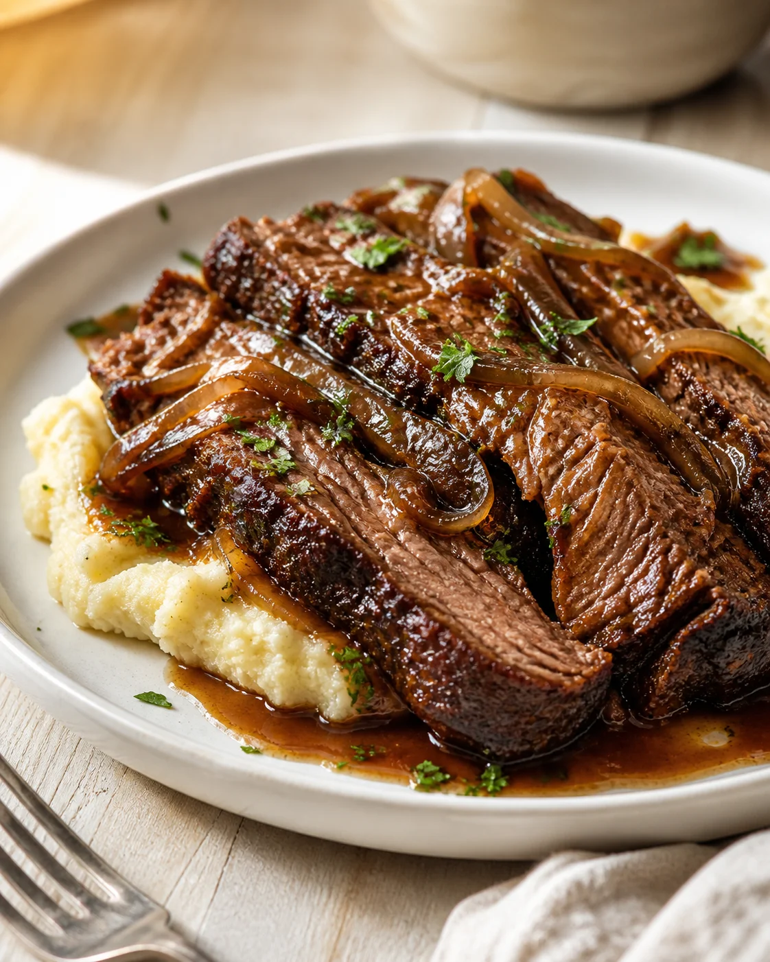 braised-beef-on-mashed-potatoes Sliced braised beef with caramelized onions on creamy mashed potatoes, drizzled with brown gravy.