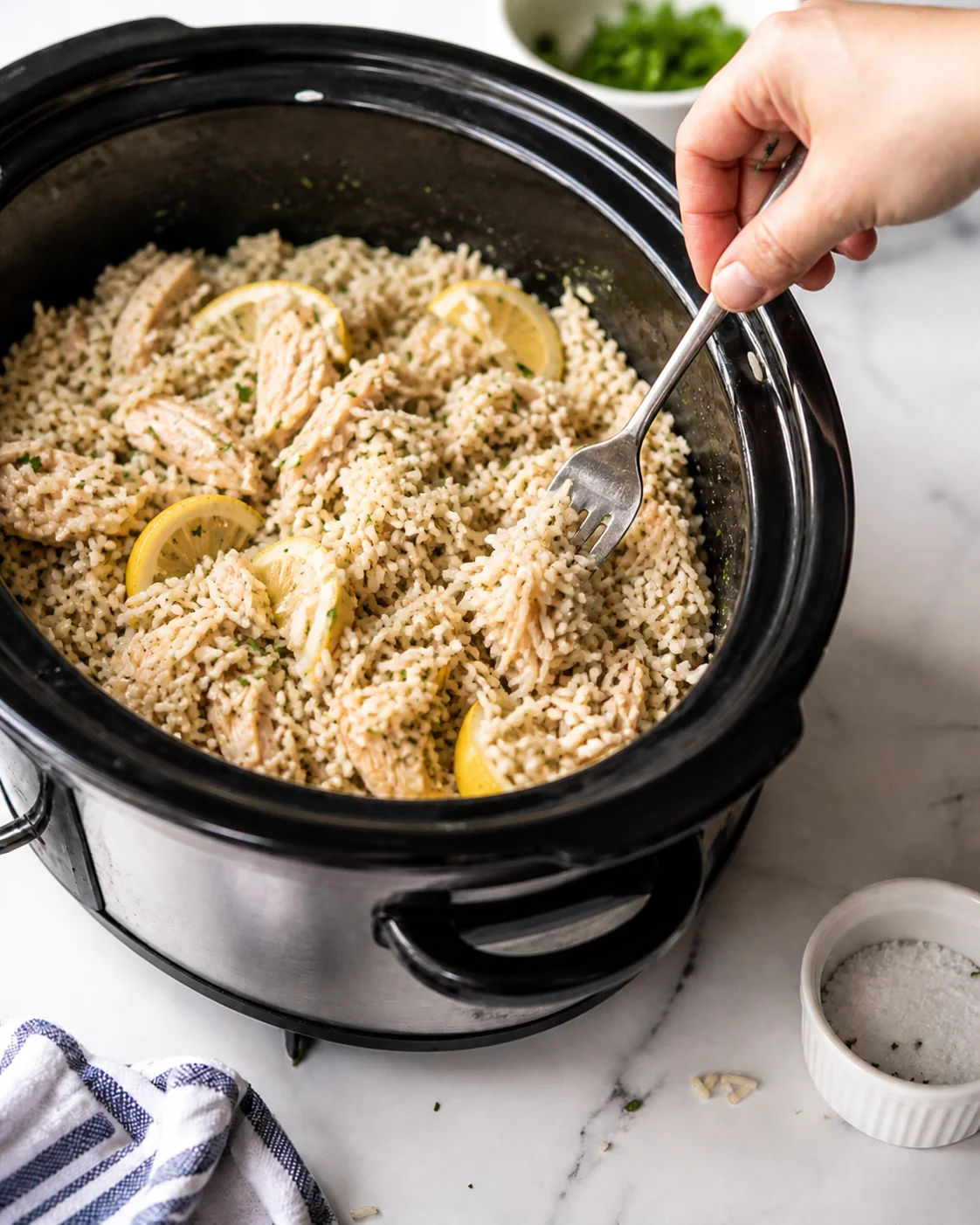 slow-cooker-lemon-chicken-rice hand stirs lemon-chicken-rice in a black slow cooker with a fork