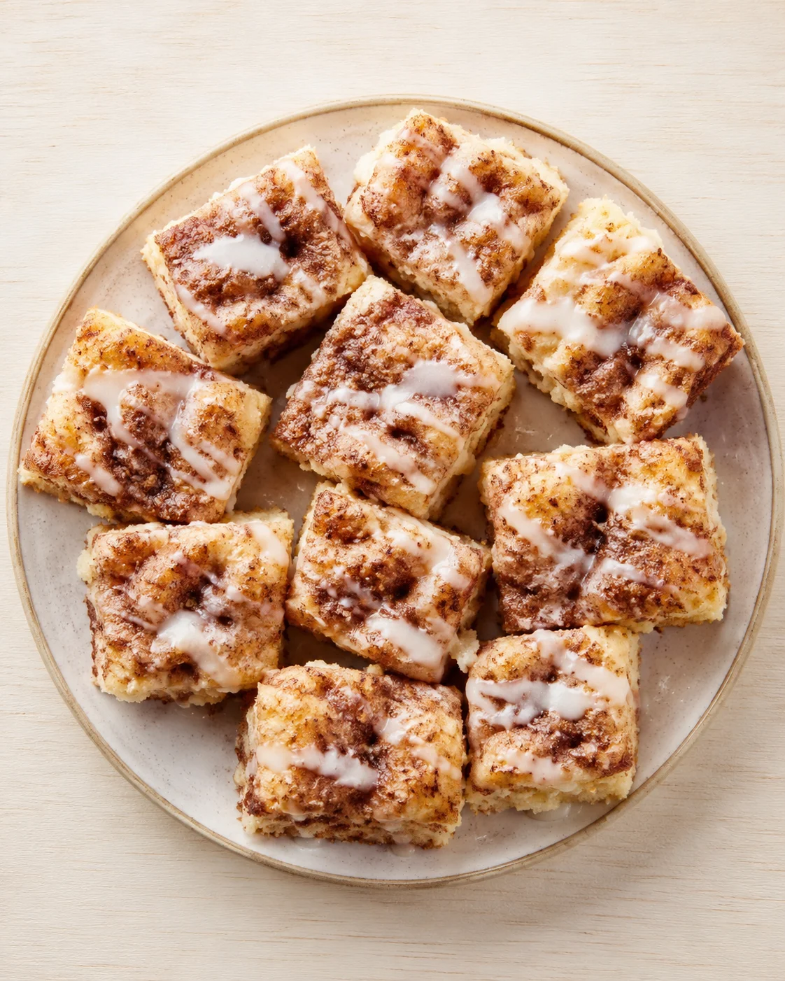 round plate with square cinnamon-sugar cake pieces drizzled with icing on a light wooden table