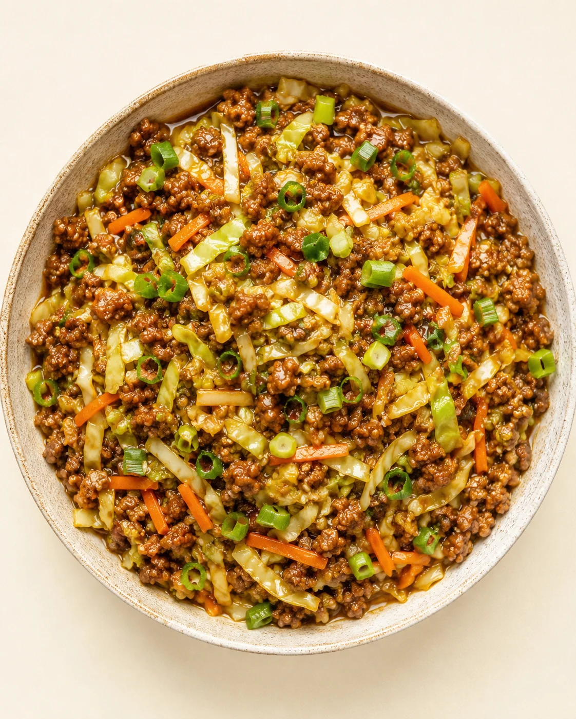 top-down view of a round ceramic bowl with minced beef, cabbage, carrots, and green onions in a glossy sauce.