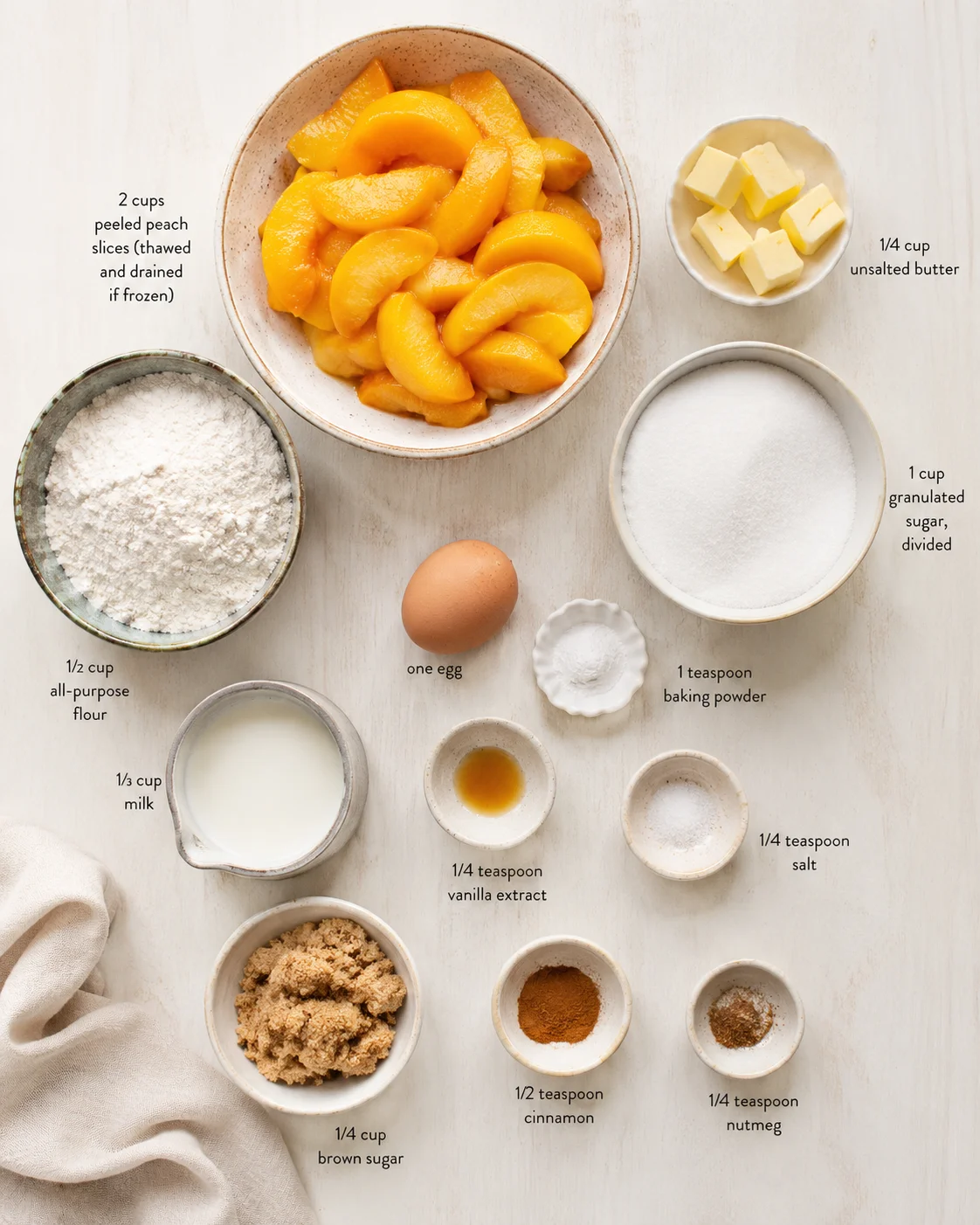 Top-down flat lay of peeled peach slices with bowls of flour, sugar, butter, and spices on a light wood surface