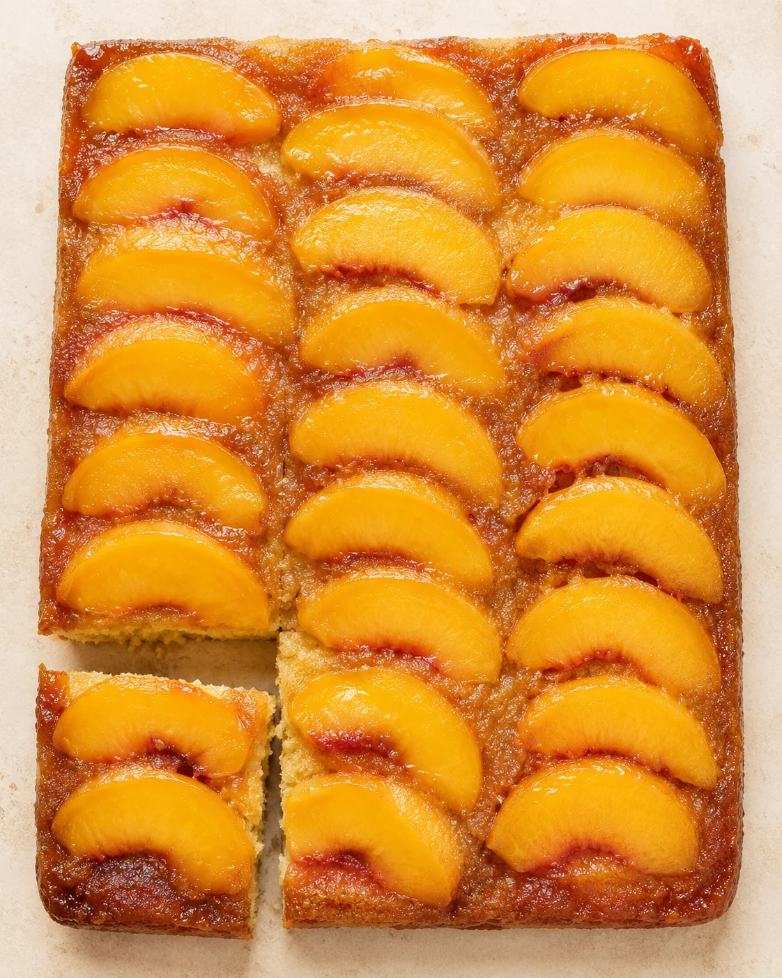 top-down view of a square peach cake with glossy glaze and neatly arranged peach slices