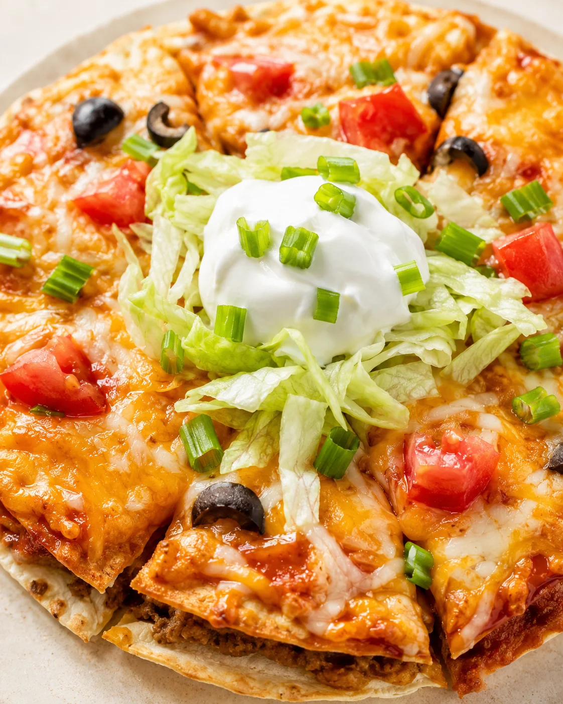 Pizza topped with lettuce, sour cream, green onions, tomatoes, and olives on melted cheese.