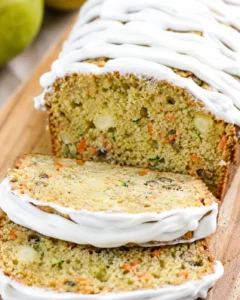 Slice of carrot-zucchini loaf cake with white cream-cheese frosting on a wooden board.
