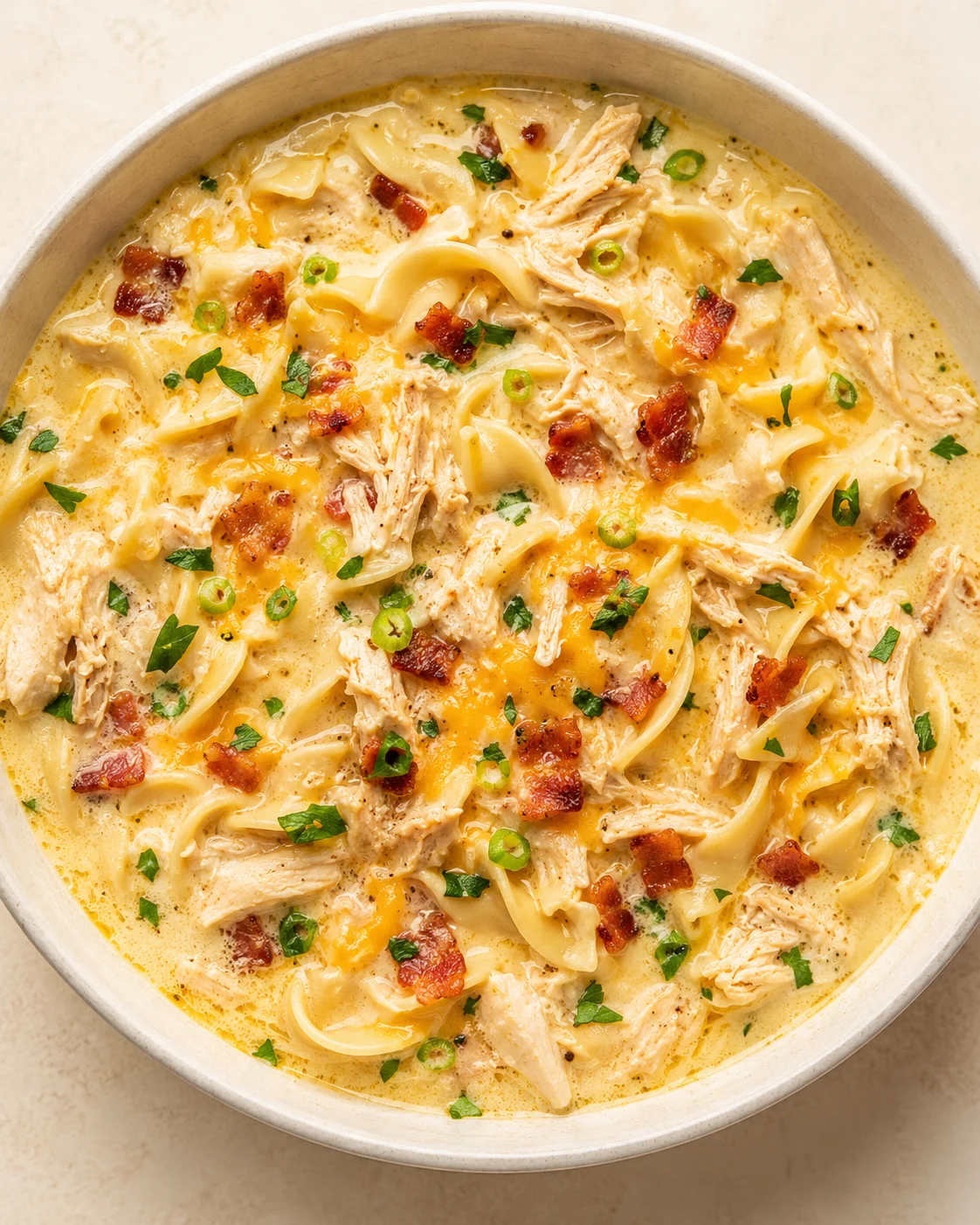 bowl of creamy chicken alfredo pasta with shredded chicken, bacon bits, and green onions.