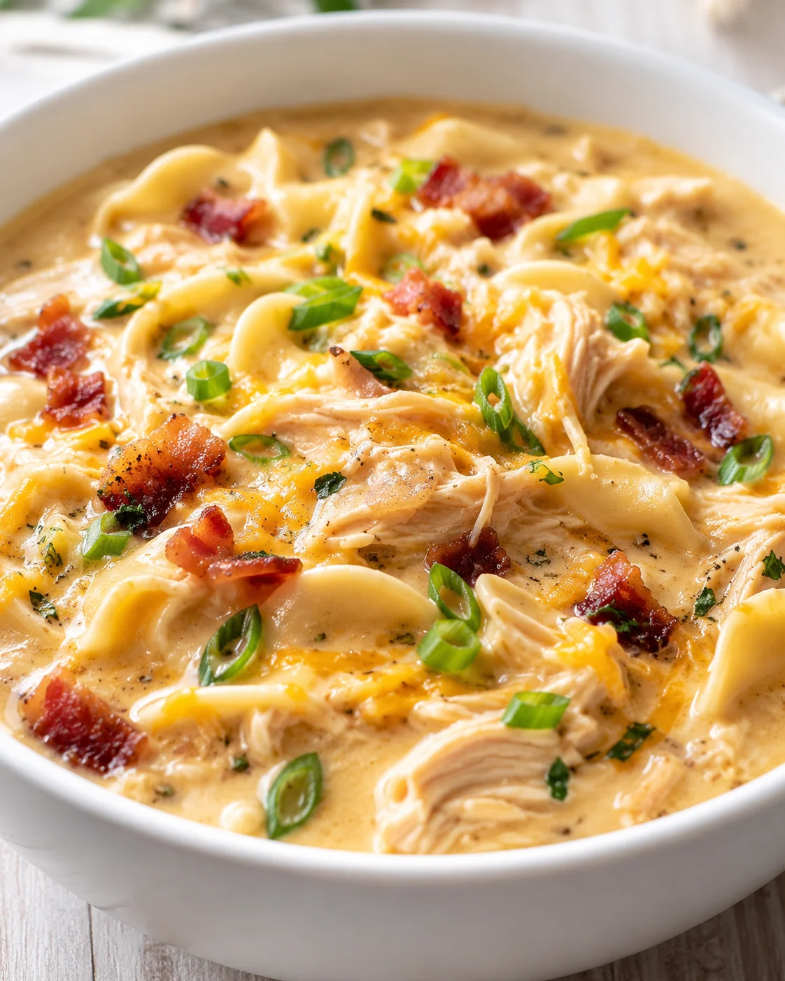 bowl of creamy chicken pasta with bacon, green onions, and herbs