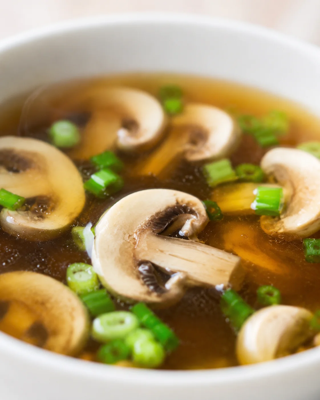 Close-up of mushroom soup with sliced mushrooms and green onions in a brown broth.
