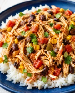 Shredded chicken with black beans, corn, peppers and cilantro on white rice on a blue plate