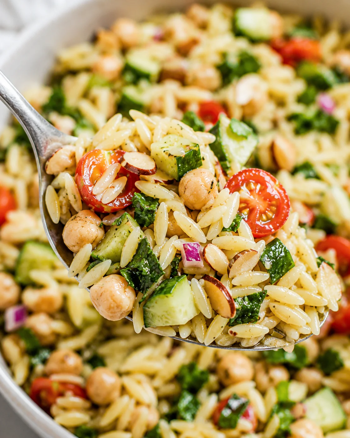 Colorful lemon orzo chickpea salad with fresh vegetables and herbs in a bowl