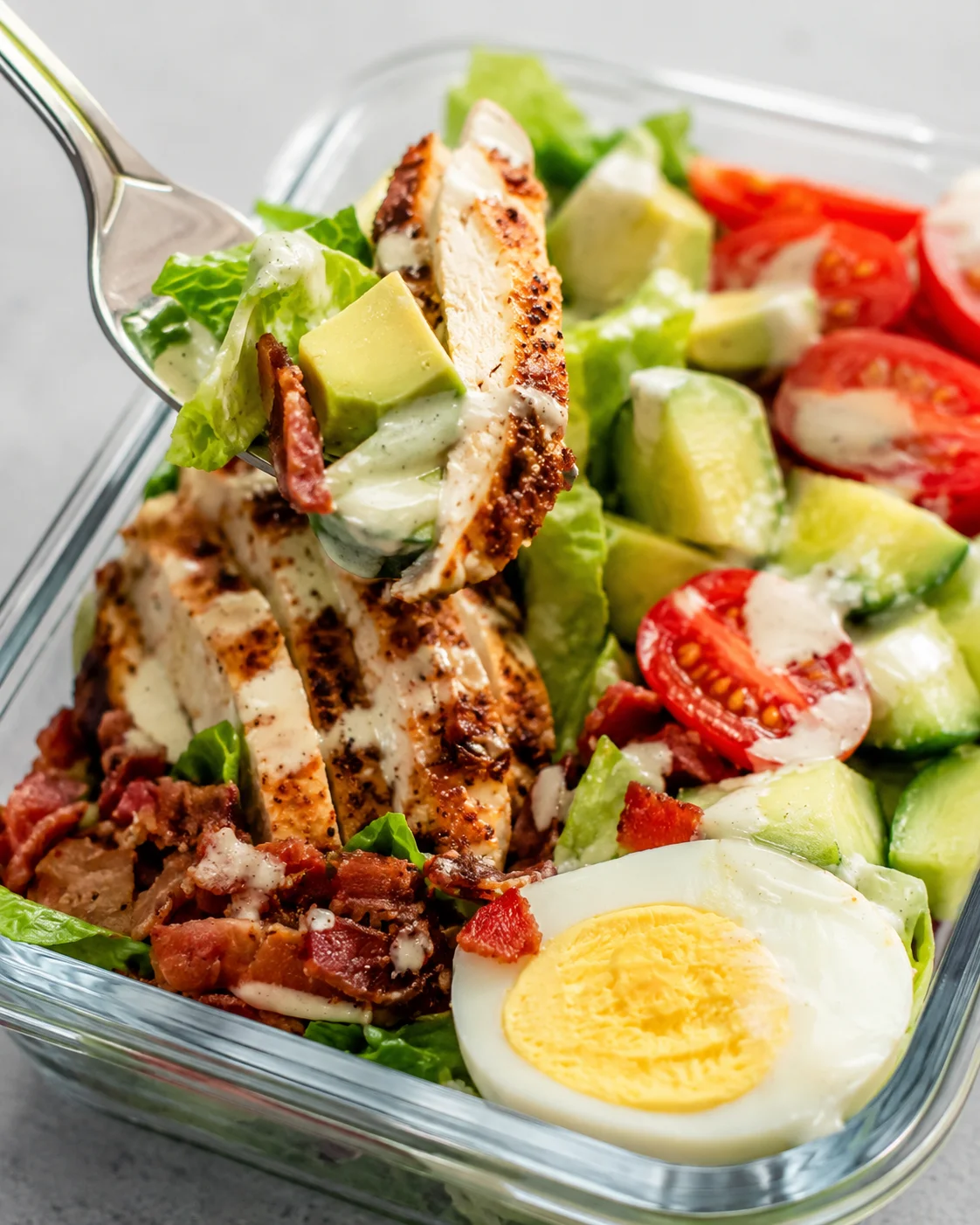 Colorful prepared Cobb salad with chicken, bacon, tomatoes, and eggs in a glass container