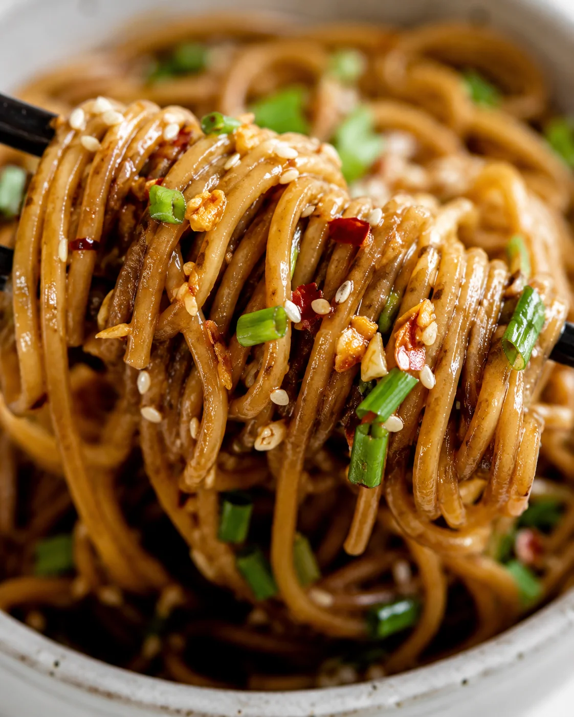 Close-up of flavorful garlic sesame noodles topped with green onions and sesame seeds.