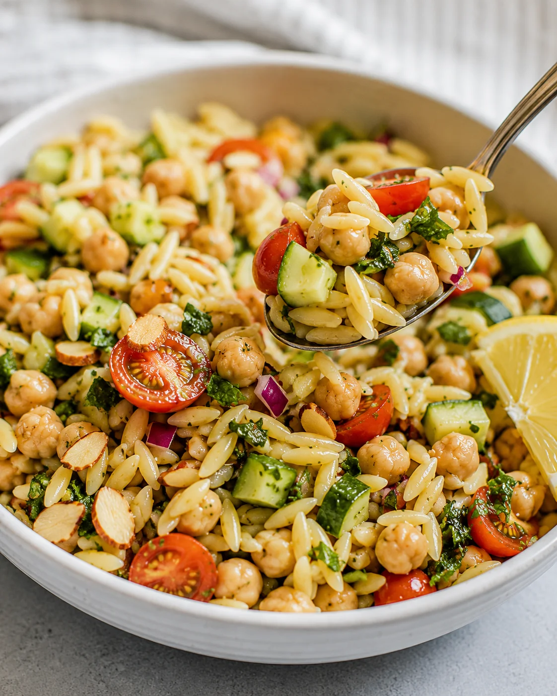 Colorful lemon orzo chickpea salad with fresh vegetables and herbs in a white bowl