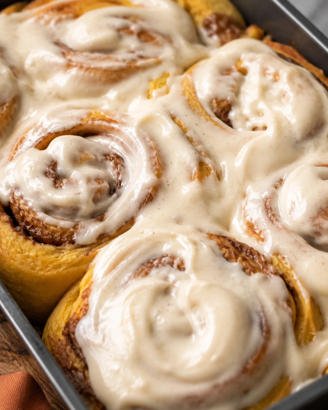 Close-up of fluffy pumpkin cinnamon rolls topped with creamy frosting in a baking dish.