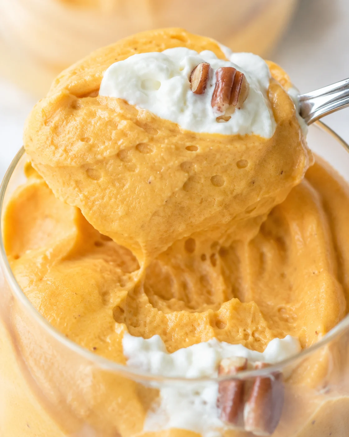 A rich, creamy pumpkin dessert served in a glass with whipped topping and pecans.