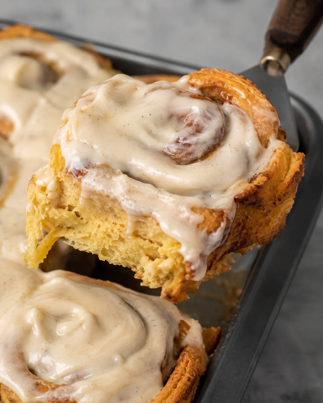Close-up of a soft, fluffy pumpkin cinnamon roll with creamy frosting.