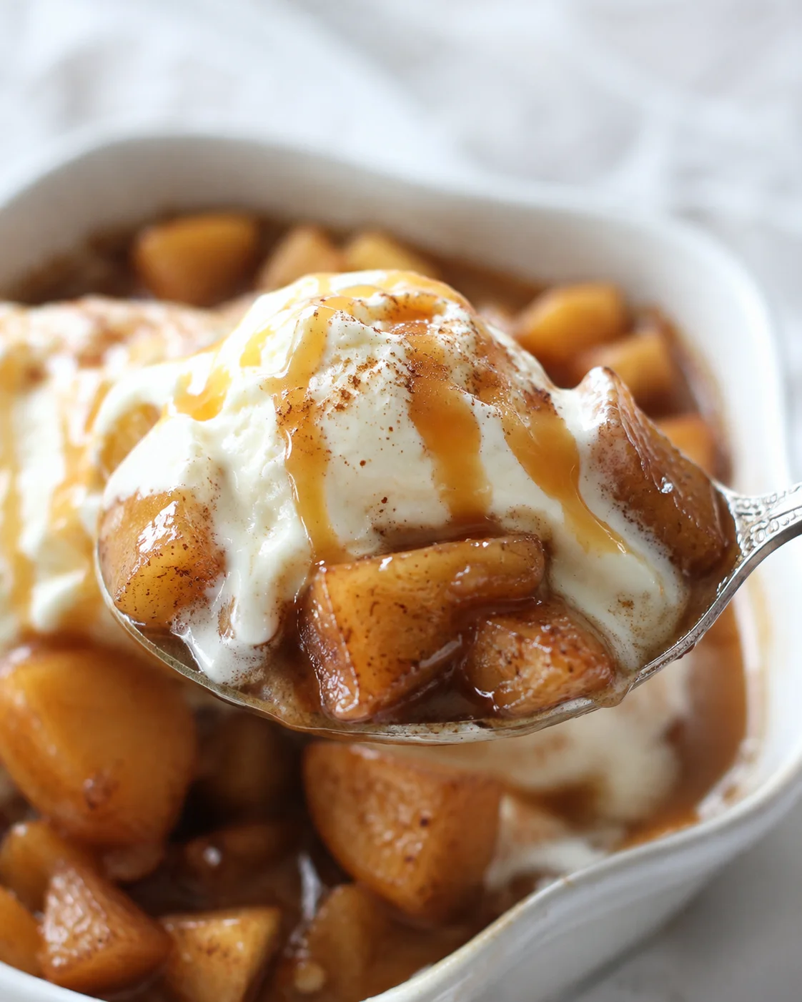Close-up of baked apple dessert topped with vanilla ice cream and caramel drizzle.