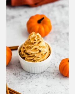 Creamy whipped pumpkin spice honey butter with pumpkins on a white surface.