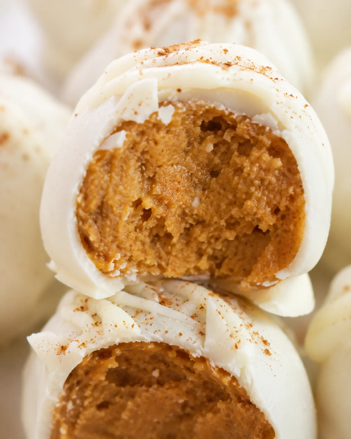 Close-up of creamy pumpkin cheesecake balls coated in white chocolate, with one bitten to show filling