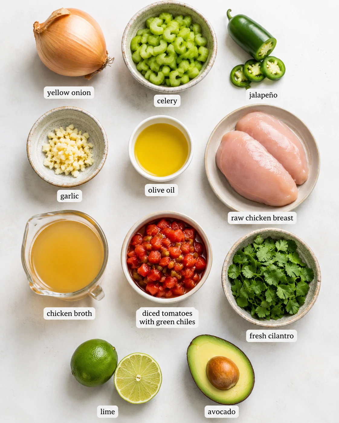 Top-down layout of ingredients for chicken and lime soup including chicken breasts, celery, jalapeño, diced tomatoes, cilantro, lime, avocado and broth