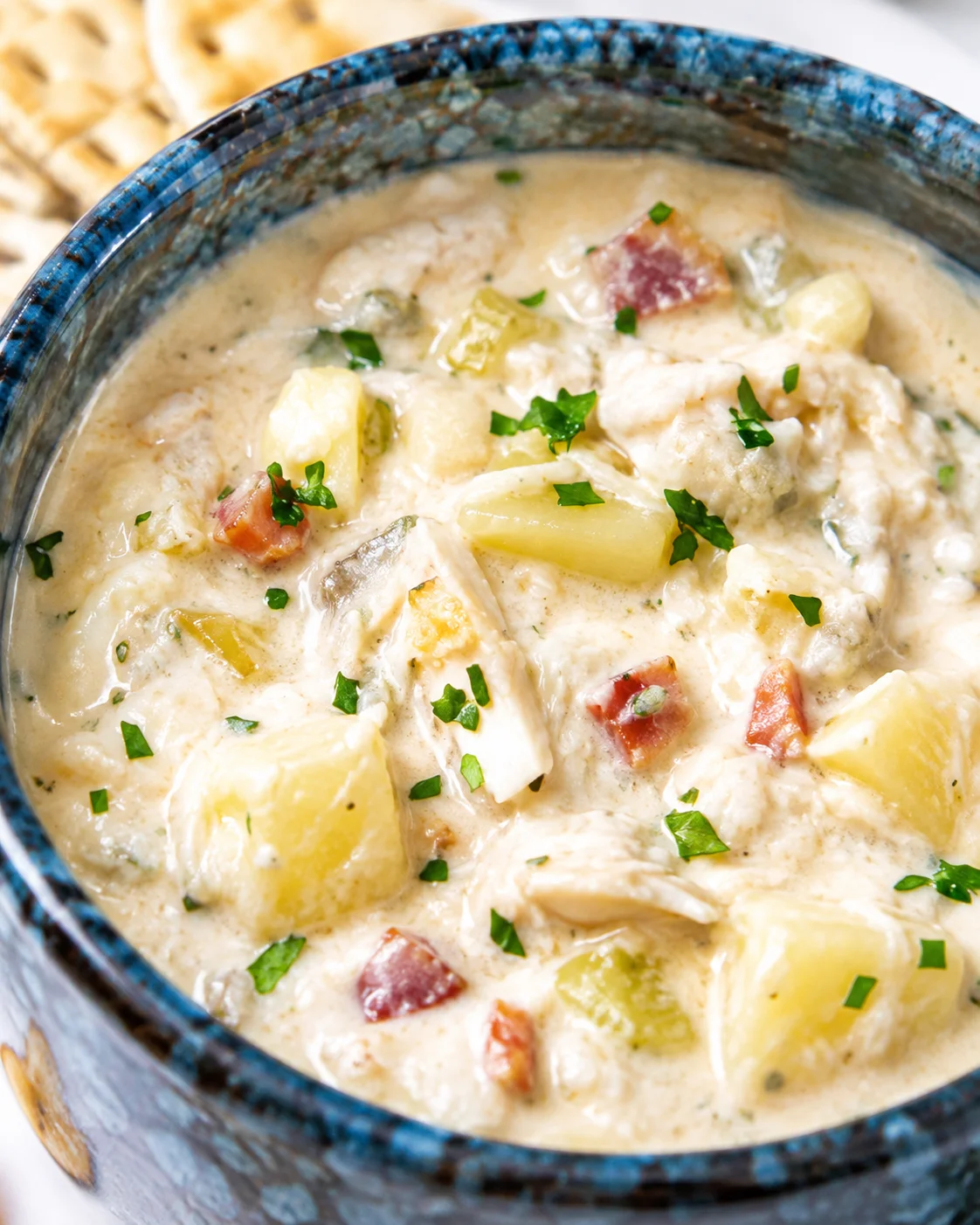 Cream of crab soup in a blue bowl with potatoes, crab meat, bacon and parsley in a creamy broth