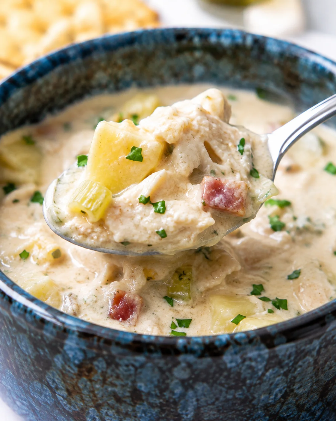 Spoon lifting a heaping bite of cream of crab soup with potato, celery and crab over a bowl