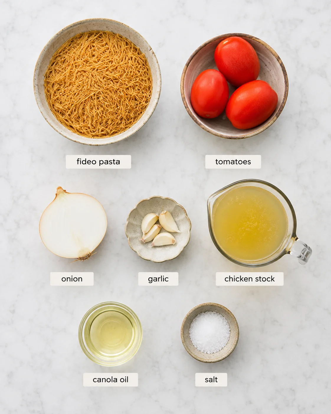 Top-down arrangement of fideo pasta, tomatoes, onion, garlic, stock, oil, and salt