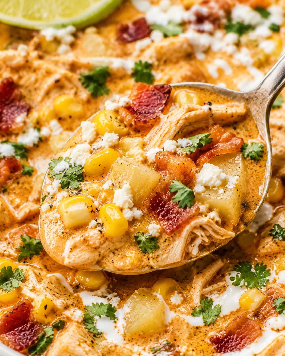 Ladle lifting a spoonful of Mexican street corn soup with potatoes, corn, shredded chicken and bacon