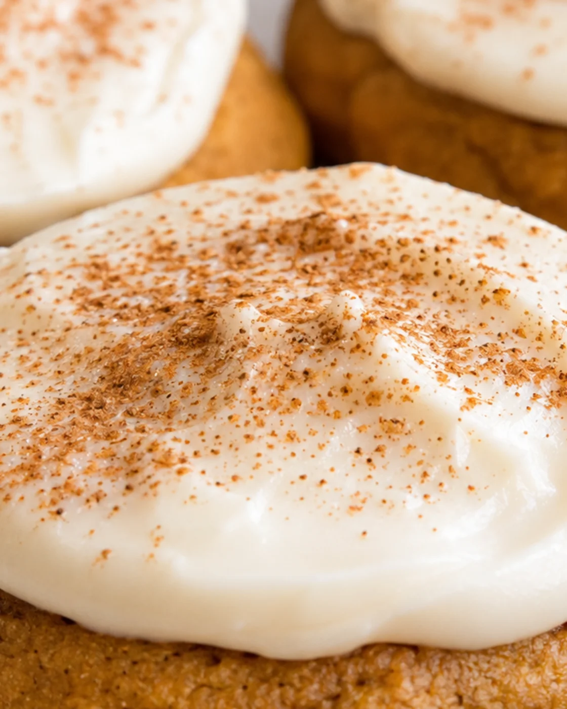 Close-up of soft pumpkin cookies topped with cream cheese frosting and sprinkled with spices.